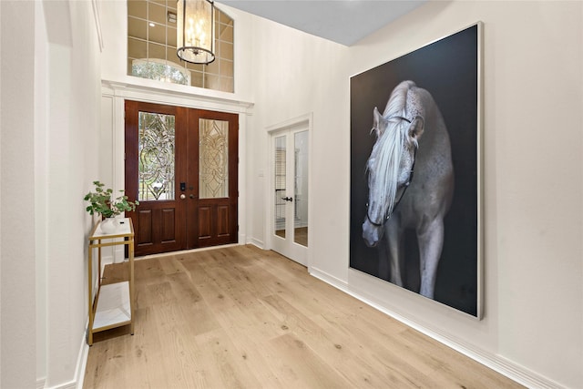 foyer with a chandelier, french doors, a towering ceiling, and light hardwood / wood-style flooring