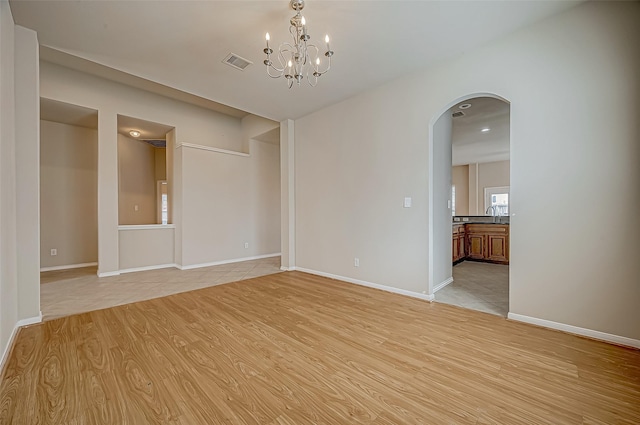 empty room with a notable chandelier and light hardwood / wood-style floors