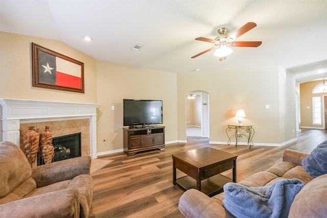 living room with wood-type flooring, ceiling fan, and a tiled fireplace