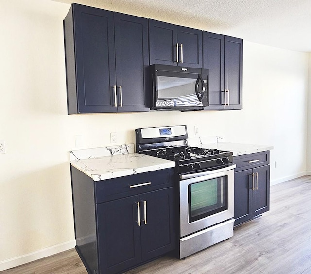 kitchen featuring stainless steel gas range oven, light stone counters, a textured ceiling, and light hardwood / wood-style flooring