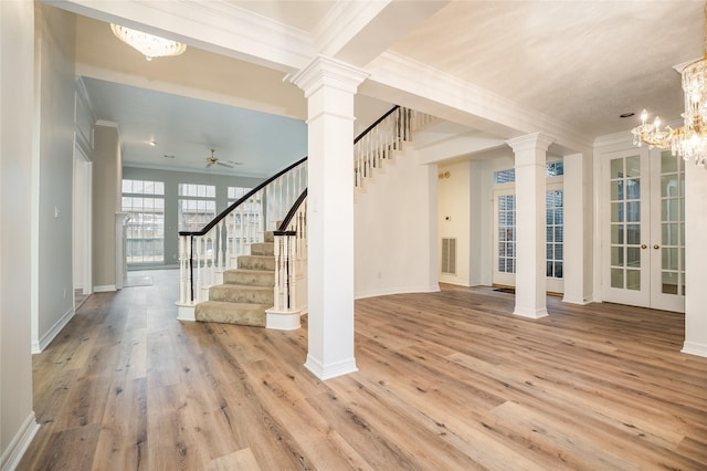 foyer entrance with french doors, ceiling fan with notable chandelier, ornate columns, light wood-type flooring, and ornamental molding