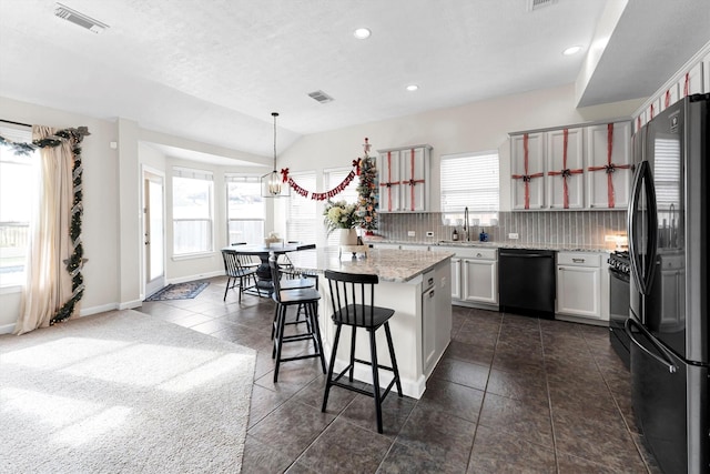 kitchen with backsplash, hanging light fixtures, vaulted ceiling, a breakfast bar, and black appliances