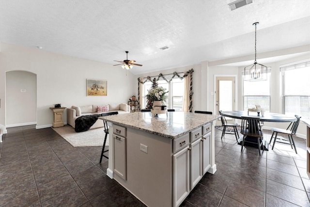 kitchen featuring a kitchen bar, decorative light fixtures, light stone countertops, ceiling fan with notable chandelier, and a center island