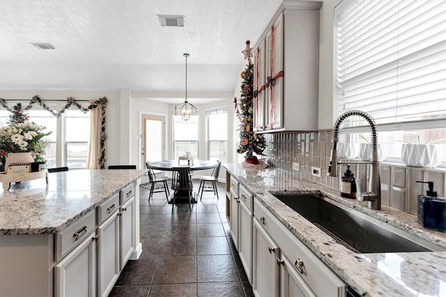 kitchen featuring hanging light fixtures, a wealth of natural light, backsplash, and sink