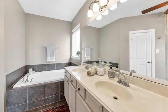 bathroom featuring ceiling fan with notable chandelier, a relaxing tiled tub, and vanity