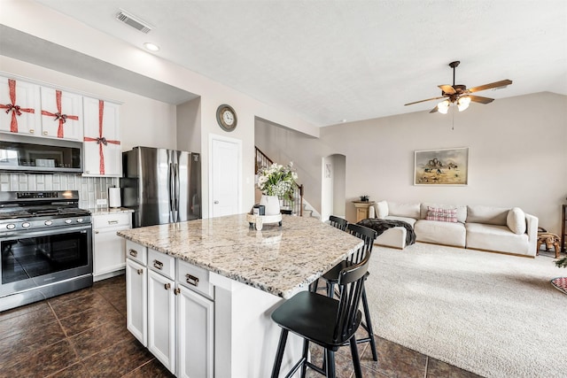 kitchen featuring white cabinets, appliances with stainless steel finishes, a center island, a kitchen bar, and decorative backsplash