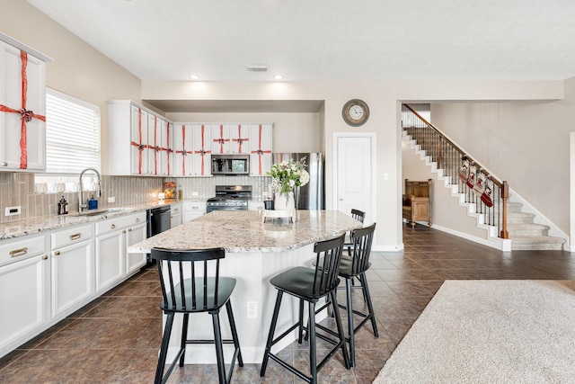 kitchen with light stone countertops, a kitchen island, white cabinetry, stainless steel appliances, and sink