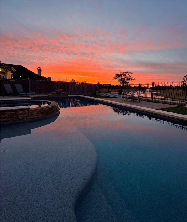 pool at dusk featuring an in ground hot tub and a patio