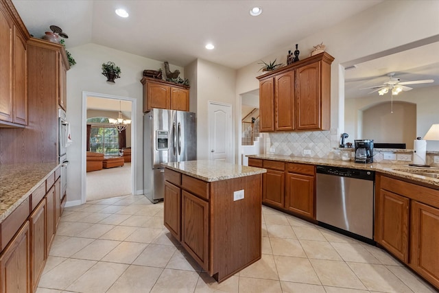 kitchen featuring lofted ceiling, decorative backsplash, a kitchen island, light stone counters, and stainless steel appliances