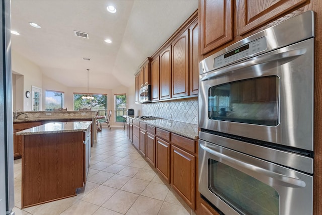 kitchen with appliances with stainless steel finishes, tasteful backsplash, light stone counters, a center island, and lofted ceiling