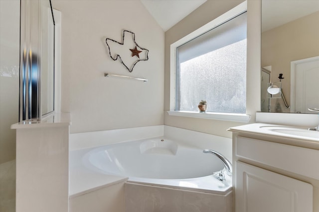 bathroom with tiled bath, vanity, and lofted ceiling