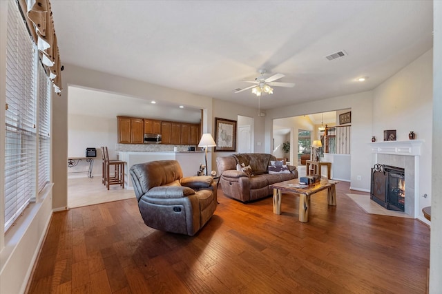 living room with hardwood / wood-style flooring, ceiling fan, and a tiled fireplace