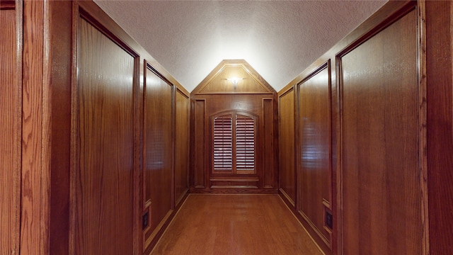 corridor featuring a textured ceiling, wood walls, lofted ceiling, and hardwood / wood-style flooring