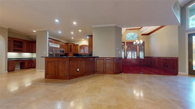 kitchen featuring kitchen peninsula, built in appliances, crown molding, and a notable chandelier