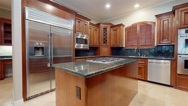 kitchen with crown molding, sink, light tile patterned floors, built in appliances, and a kitchen island