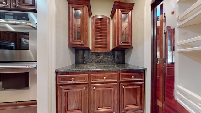 kitchen with tasteful backsplash, dark stone counters, and stainless steel double oven