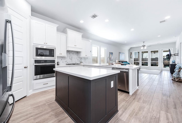 kitchen with a center island, tasteful backsplash, white cabinets, appliances with stainless steel finishes, and ceiling fan