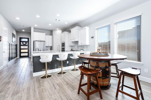 kitchen with a kitchen breakfast bar, a center island with sink, stainless steel appliances, decorative backsplash, and white cabinets