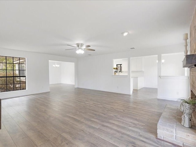 unfurnished living room featuring ceiling fan with notable chandelier, a brick fireplace, and wood finished floors