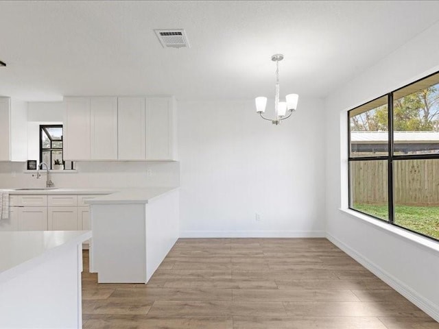 unfurnished dining area featuring a notable chandelier, visible vents, light wood-style flooring, and a sink