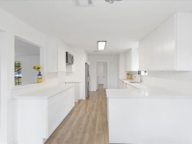 kitchen featuring visible vents, light wood-style flooring, a sink, appliances with stainless steel finishes, and light countertops