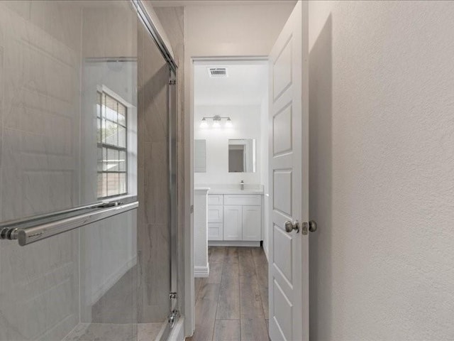 full bathroom with vanity, wood finished floors, visible vents, a shower stall, and a textured wall