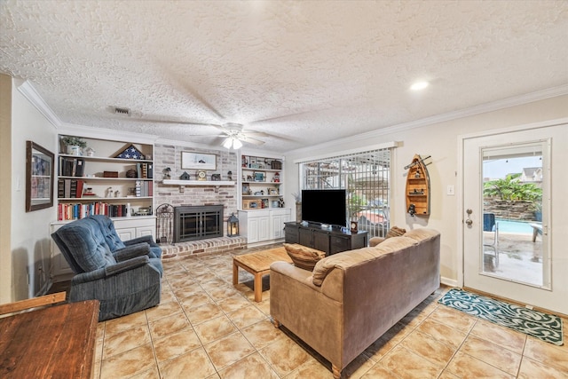 tiled living room featuring built in shelves, ceiling fan, a brick fireplace, a textured ceiling, and ornamental molding