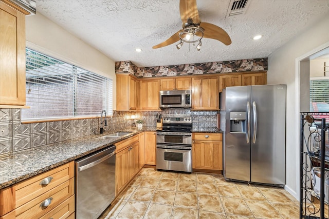 kitchen featuring a textured ceiling, sink, stainless steel appliances, and dark stone counters