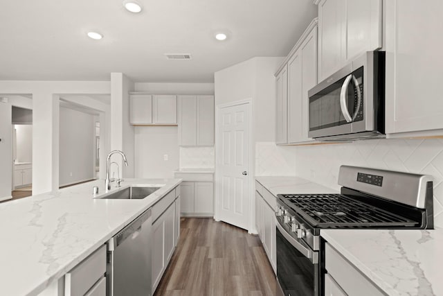 kitchen with backsplash, white cabinets, sink, light stone countertops, and stainless steel appliances