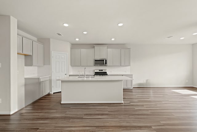 kitchen featuring sink, stainless steel appliances, backsplash, an island with sink, and hardwood / wood-style flooring