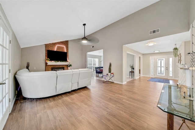 living room with a brick fireplace, light hardwood / wood-style flooring, and vaulted ceiling