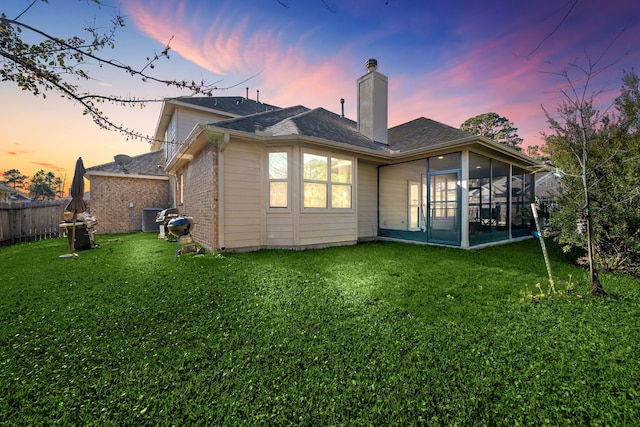 back house at dusk featuring a lawn and a sunroom