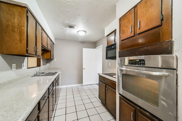 kitchen with oven, sink, a textured ceiling, light tile patterned flooring, and electric stovetop