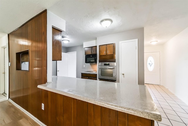 kitchen with kitchen peninsula, stainless steel oven, cooktop, a textured ceiling, and light tile patterned flooring