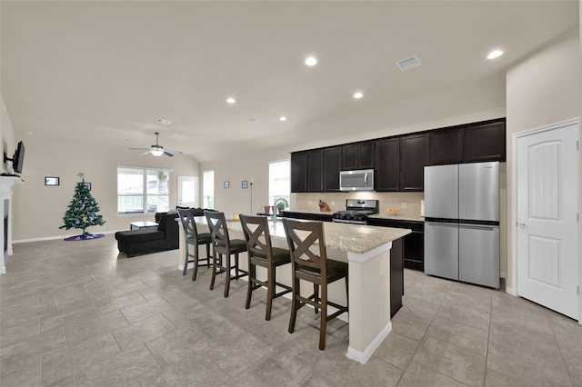 kitchen featuring a kitchen breakfast bar, light stone counters, stainless steel appliances, ceiling fan, and an island with sink