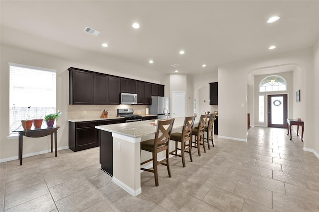 kitchen featuring a breakfast bar area, light stone counters, a center island with sink, and stainless steel appliances