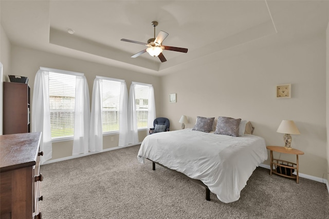 carpeted bedroom with a raised ceiling and ceiling fan