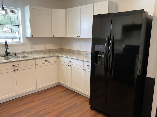 kitchen featuring sink, wood-type flooring, light stone countertops, white cabinets, and black refrigerator with ice dispenser