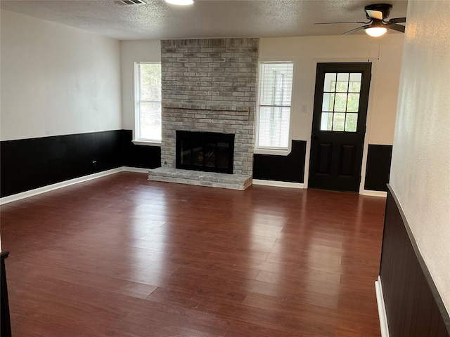 unfurnished living room featuring ceiling fan, dark hardwood / wood-style floors, a textured ceiling, and a wealth of natural light