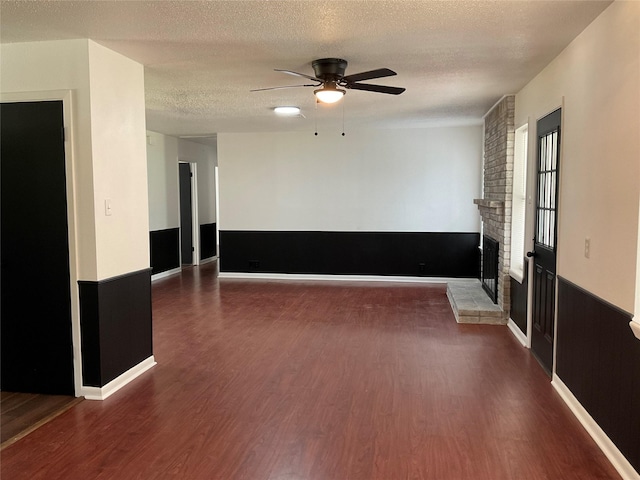 empty room with a brick fireplace, dark hardwood / wood-style floors, a textured ceiling, and ceiling fan