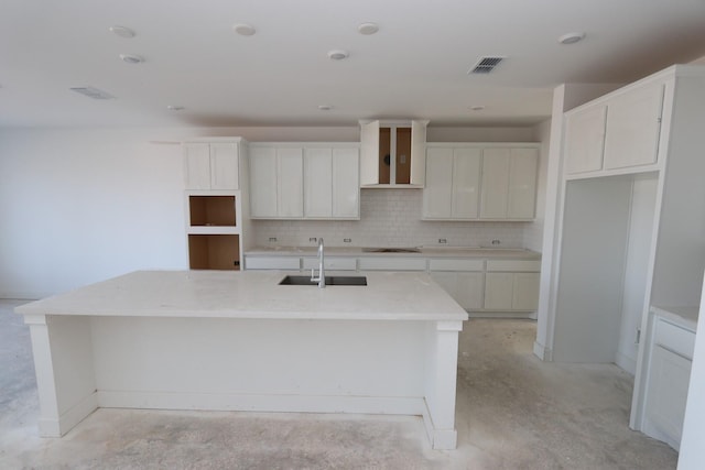 kitchen with decorative backsplash, wall chimney exhaust hood, a kitchen island with sink, sink, and white cabinetry