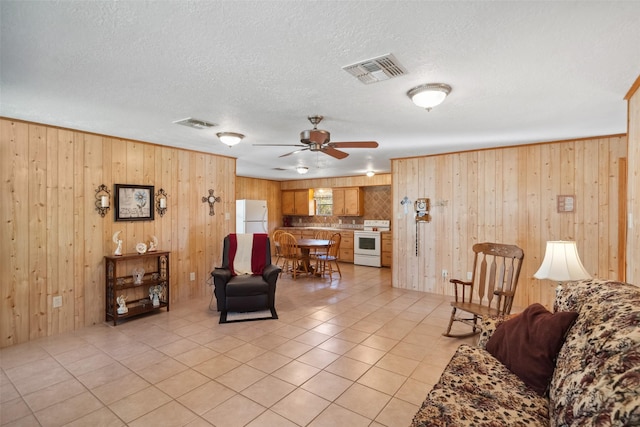 living room featuring ceiling fan, wooden walls, a textured ceiling, and light tile patterned floors