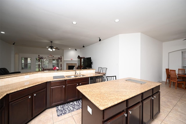 kitchen with ceiling fan, sink, a center island, light stone counters, and light tile patterned floors