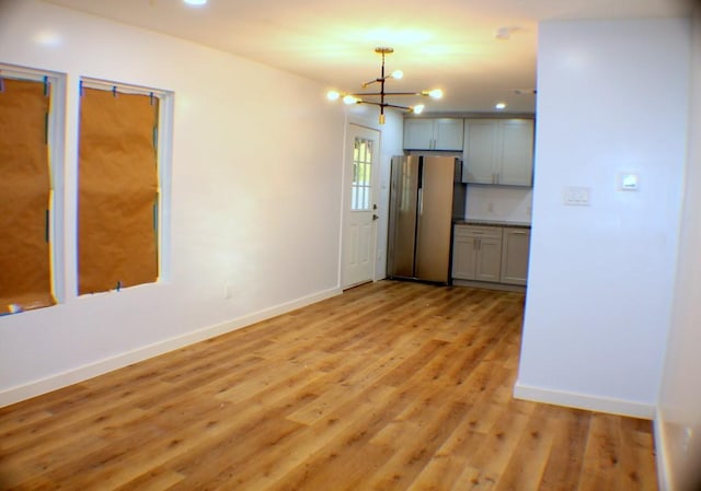 interior space featuring stainless steel fridge, light wood-type flooring, gray cabinetry, decorative light fixtures, and a chandelier