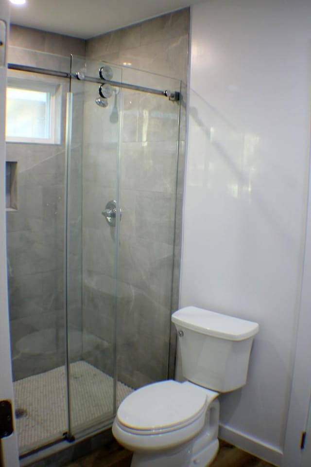 bathroom with toilet, wood-type flooring, and a shower with shower door