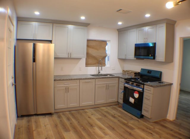 kitchen featuring stone counters, sink, light hardwood / wood-style flooring, and appliances with stainless steel finishes