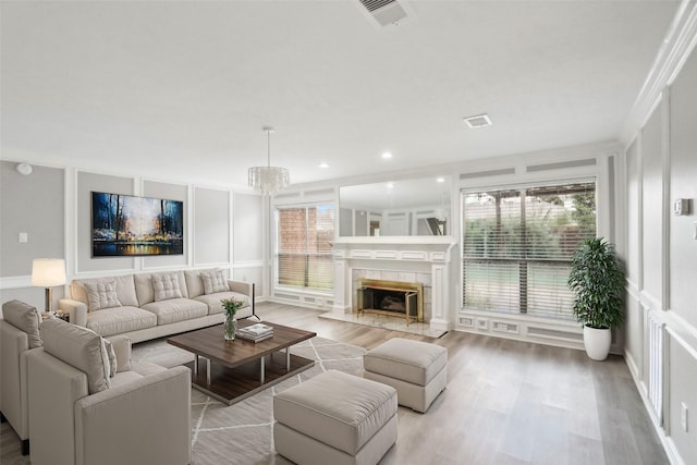 living room with a fireplace, a chandelier, light hardwood / wood-style flooring, and crown molding