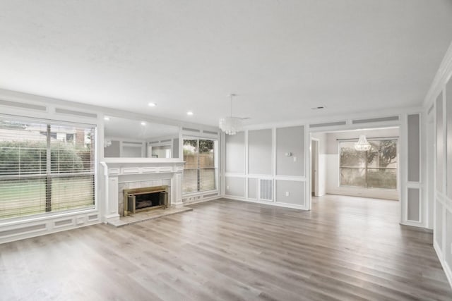 unfurnished living room featuring hardwood / wood-style floors, an inviting chandelier, crown molding, and a tiled fireplace