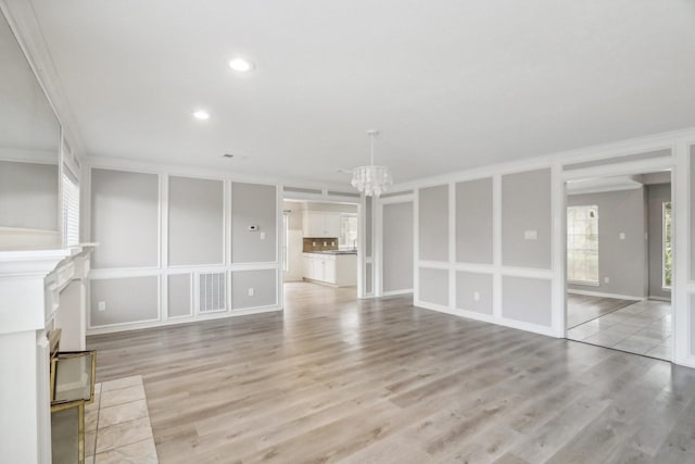 unfurnished living room featuring a chandelier, light hardwood / wood-style flooring, and ornamental molding