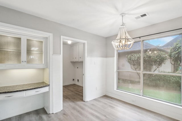 unfurnished dining area featuring a wealth of natural light, light wood-type flooring, and an inviting chandelier